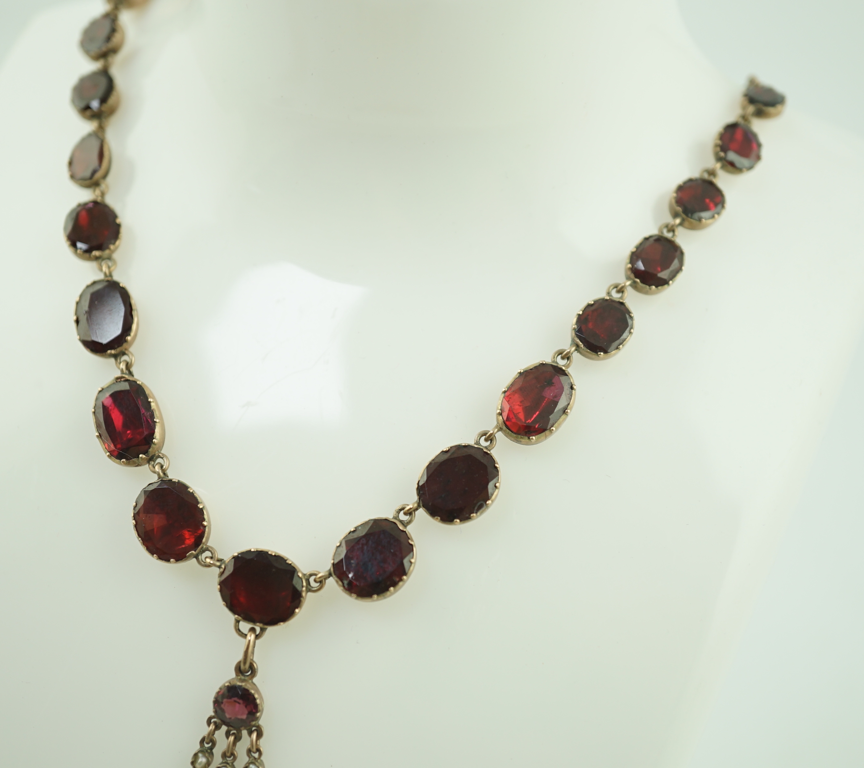 An early 19th century gold, and thirty five graduated foil backed garnet set necklace, with later garnet and seed pearl set drop